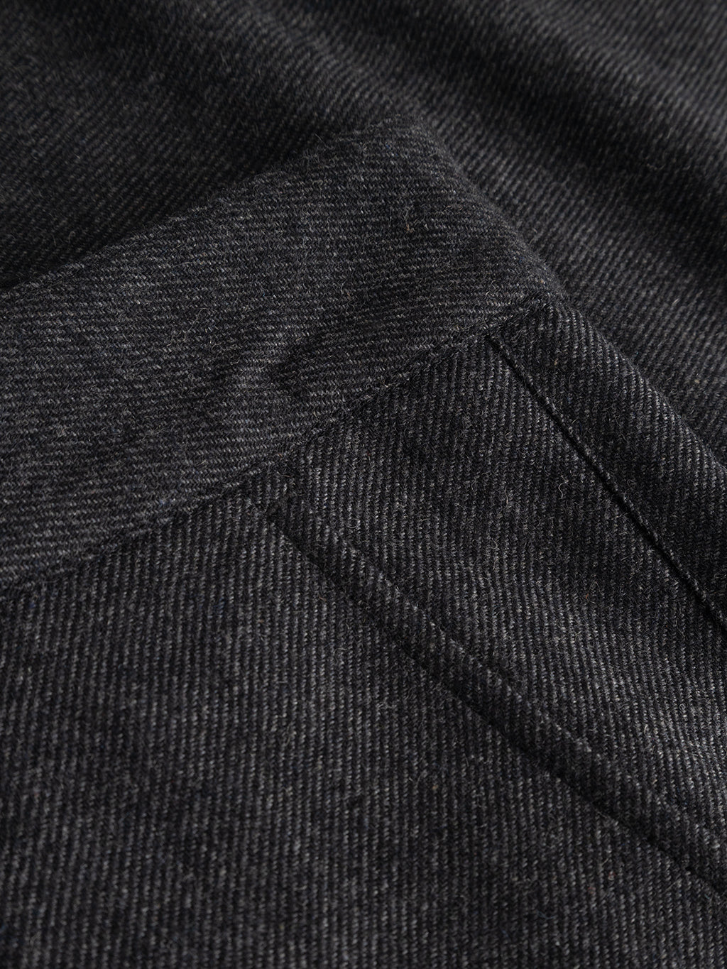 Close-up of the dark grey wool-blend twill fabric used in the Gabba GABdavid Twilight Pant, featuring a visible diagonal weave pattern and the corner of a sewn pocket. The texture and stitching highlight the contemporary design of these trousers, characterized by their loose tapered fit.