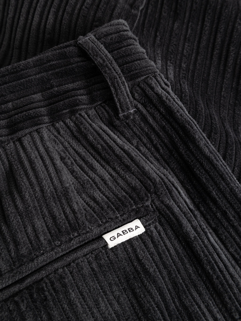 Close-up of the Gabba GABfirenze Cropped Riglia GOTS Pant in dark grey, featuring ribbed organic cotton corduroy with a relaxed fit and visible texture. A pocket with a white fabric label is also shown.
