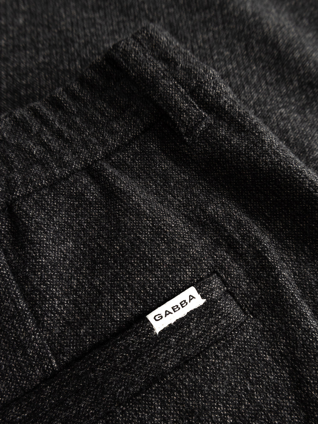 Close-up of the GABmonza Cropped Tasca Zaffe GRS Pant by Gabba in dark grey, showing its textured wool-look fabric and a small white “Gabba” label sewn into the pocket seam.
