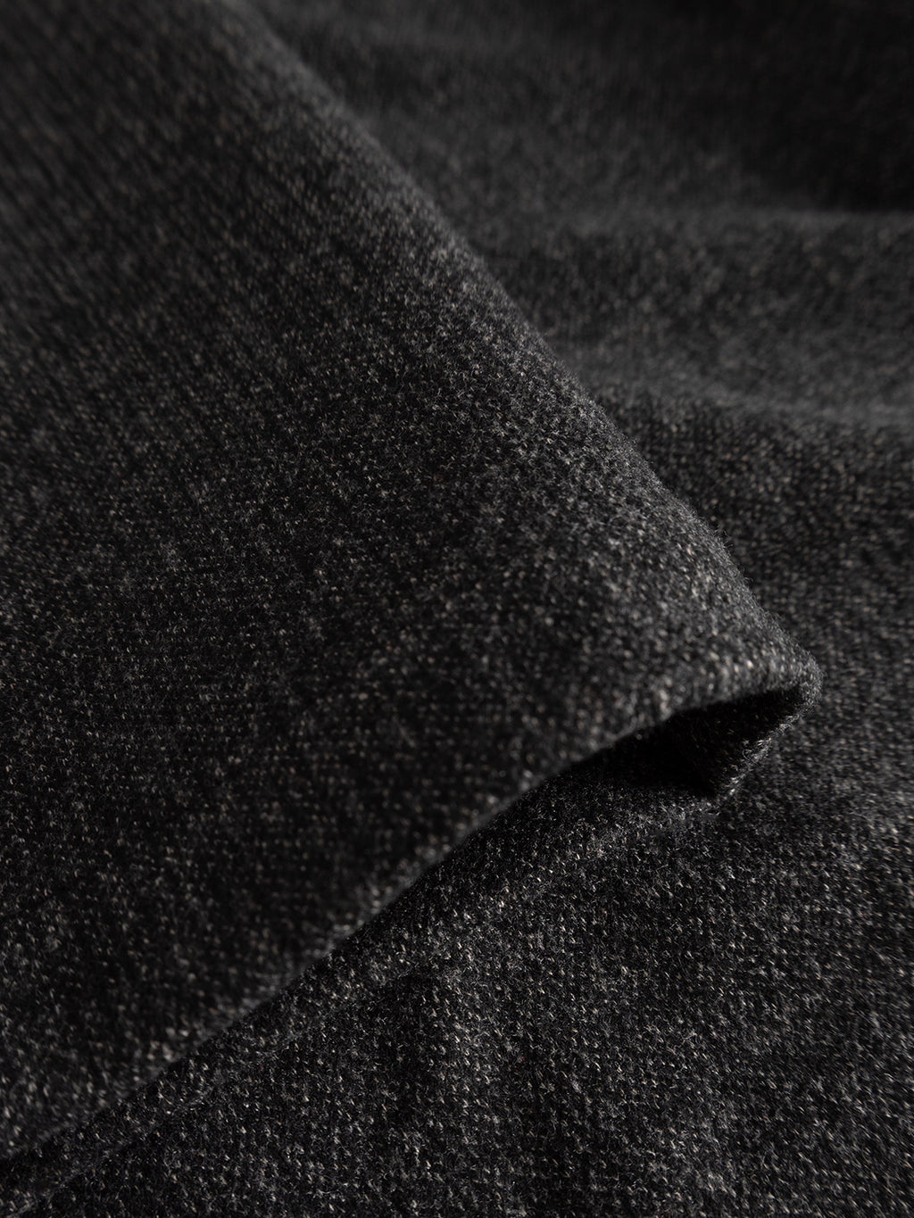 A close-up image of the Gabba GABmonza Cropped Tasca Zaffe GRS Pant in dark grey showcases the textured fabric’s intricate weave and soft, wool-look finish. The gentle folds highlight its thickness and premium material quality, making it ideal for garments with elastic waistbands or a relaxed, straight fit.