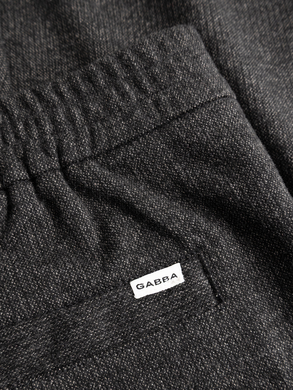 Close-up of the Gabba GABnapoli 19 Zaffe GRS Pant in dark grey, featuring an elastic waistband and a pocket adorned with a small white Gabba tag. Crafted from soft stretch fabric for comfort, these regular straight fit trousers offer a refined touch with their wool-look finish.
