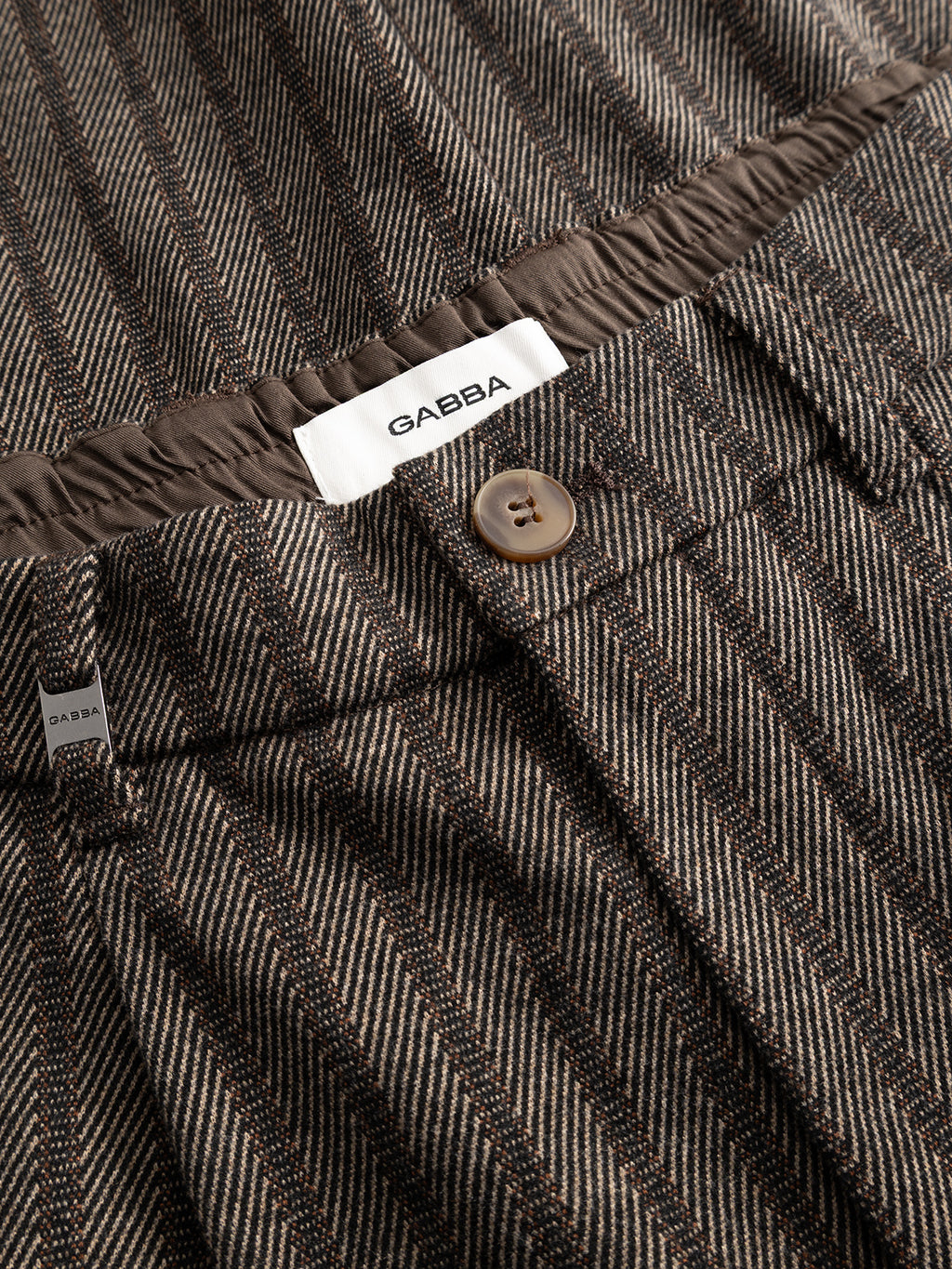 Close-up of the Gabba GABnapoli 19 Zapies Pant in Brown Slate, featuring a regular straight fit, button and waistband, and a visible Gabba label inside. The stretch fabric has a textured wool-look stripe with a diagonal pattern.
