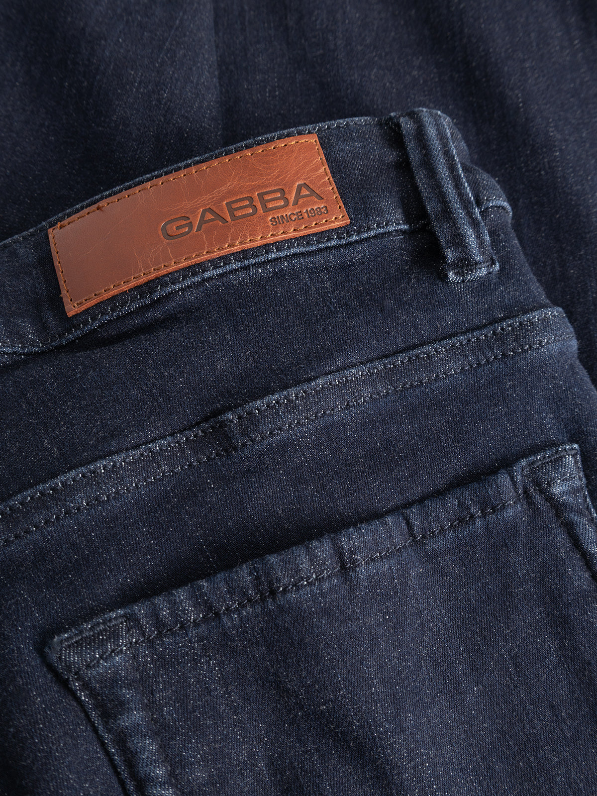 Close-up of the GABjones Vanew Rinse Jeans in dark blue denim, showcasing a brown leather patch with the Gabba brand name stitched above the back pocket. Made from ISKO superstretch denim, these slim straight fit jeans combine comfort and style.