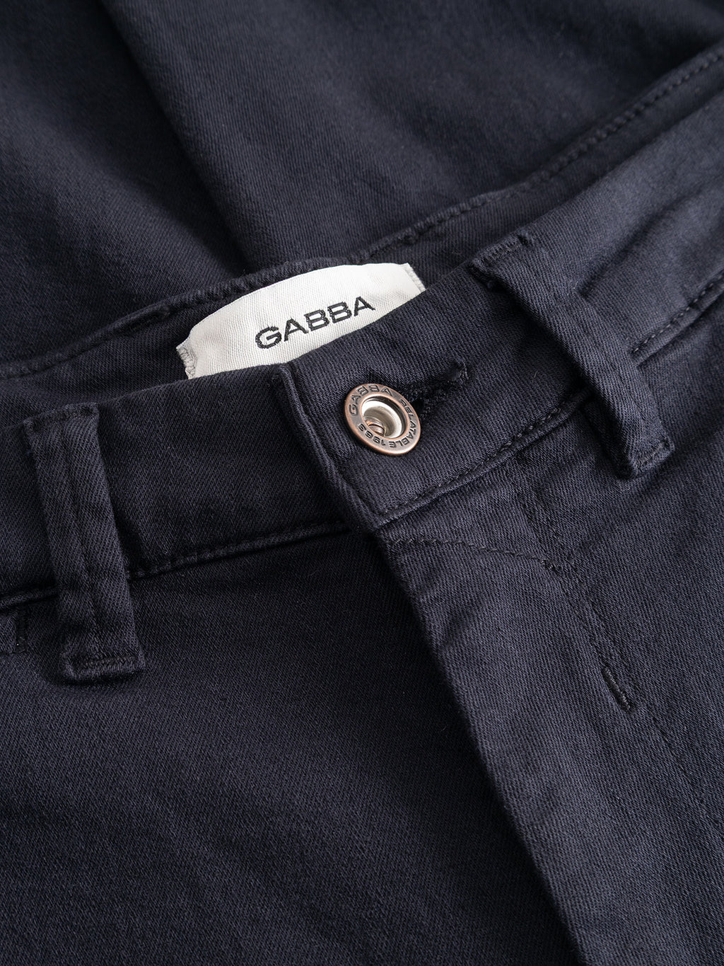 Close-up of the GABpaul Hesky Pant in Navy by Gabba, featuring a metal button and a visible white label with the brand name inside the waistband, crafted from high-stretch garment-dyed fabric for enhanced comfort.