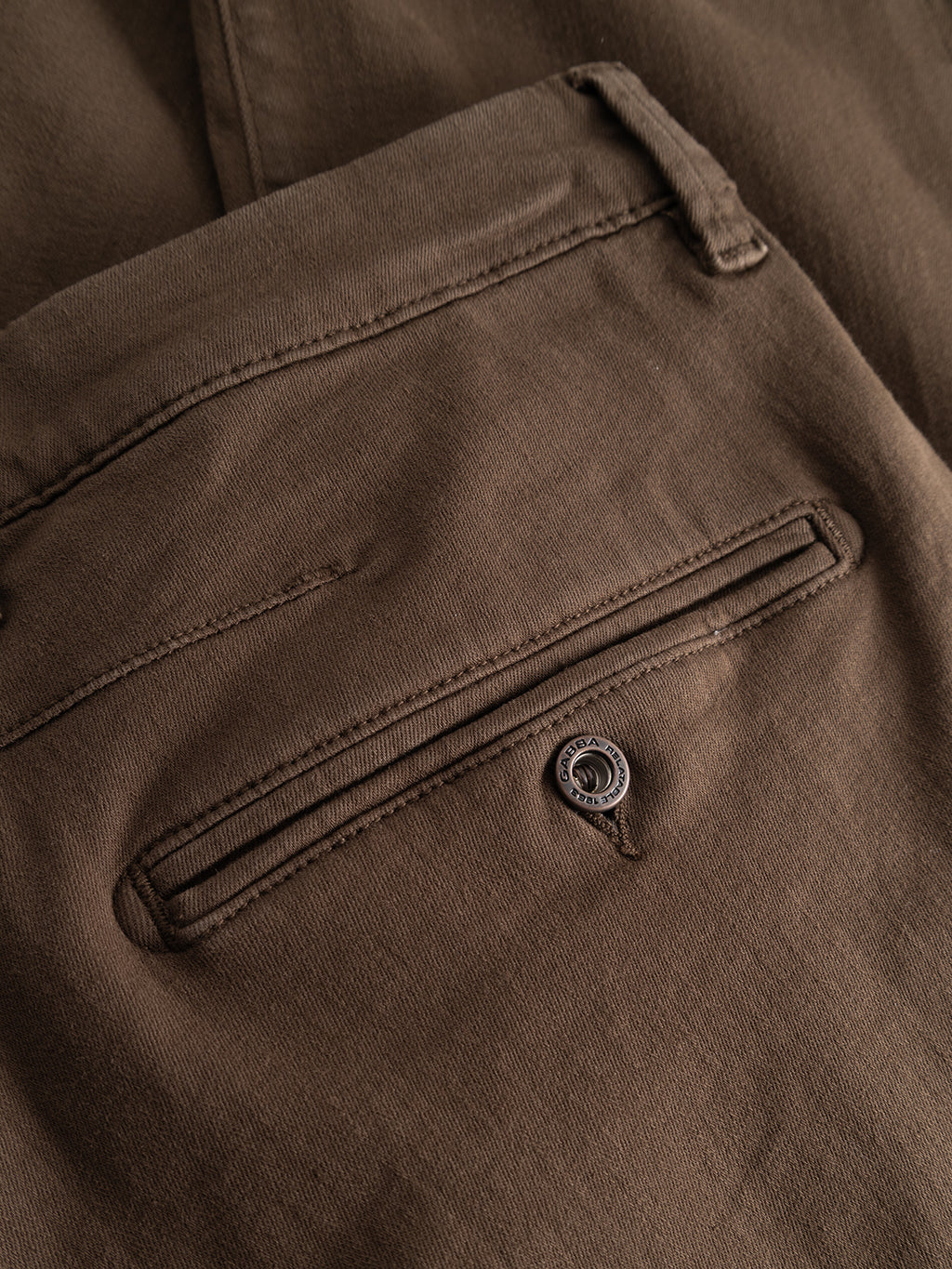 Close-up of the back pocket on the Gabba GABpaul Hesky Pant in brown, highlighting a single welt pocket with button closure and prominent stitching details. Made from high-stretch fabric, these garment-dyed pants provide exceptional comfort and durability.