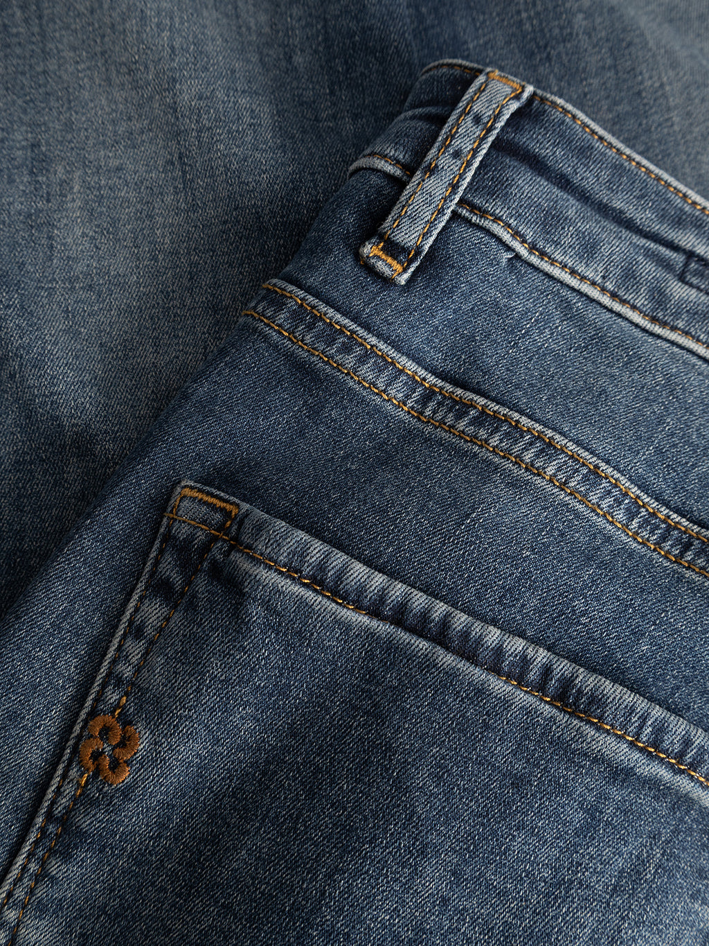 Close-up of the Gabba GABjones2 Nham RS2113 Jeans in dark blue denim, featuring a slim straight fit with visible pocket, belt loop, and yellow stitching, laid atop another piece of performance stretch denim fabric in the background.