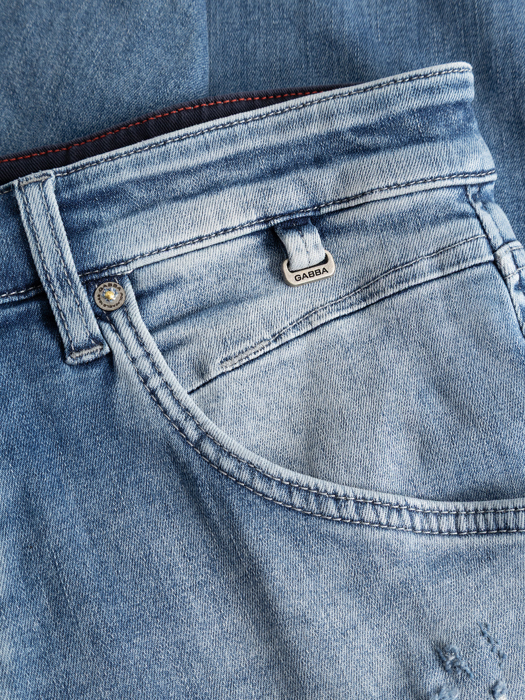 Close-up of the front pocket of the GABalex Cropped Nham RS2112 Jeans in mid blue denim by Gabba, highlighting a metal button, coin pocket, and a small tag with Gabba branding. Crafted from ISKO stretch denim for enhanced performance comfort, the fabric is slightly faded with visible stitching and features a relaxed tapered fit.