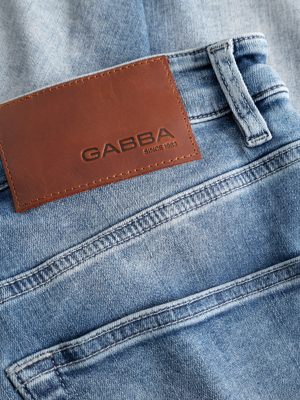 Close-up of the Gabba GABalex Cropped Nham RS2112 Jeans in mid blue denim, featuring a brown leather patch on the waistband embossed with “GABBA SINCE 1983.” Made from premium ISKO stretch denim, these jeans showcase visible stitching, back pockets, and a relaxed tapered fit that offers performance comfort.