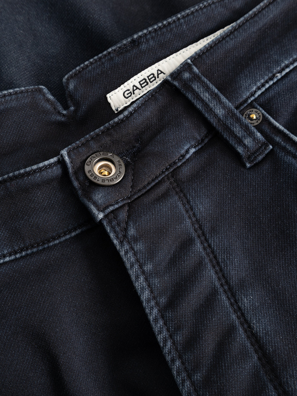 Close-up of the GABalex Cropped Torino RS2106 Jeans in dark blue denim by Gabba, featuring a visible brand label, metal button, belt loops, and detailed front pocket stitching; crafted from premium indigo denim with a relaxed tapered fit.