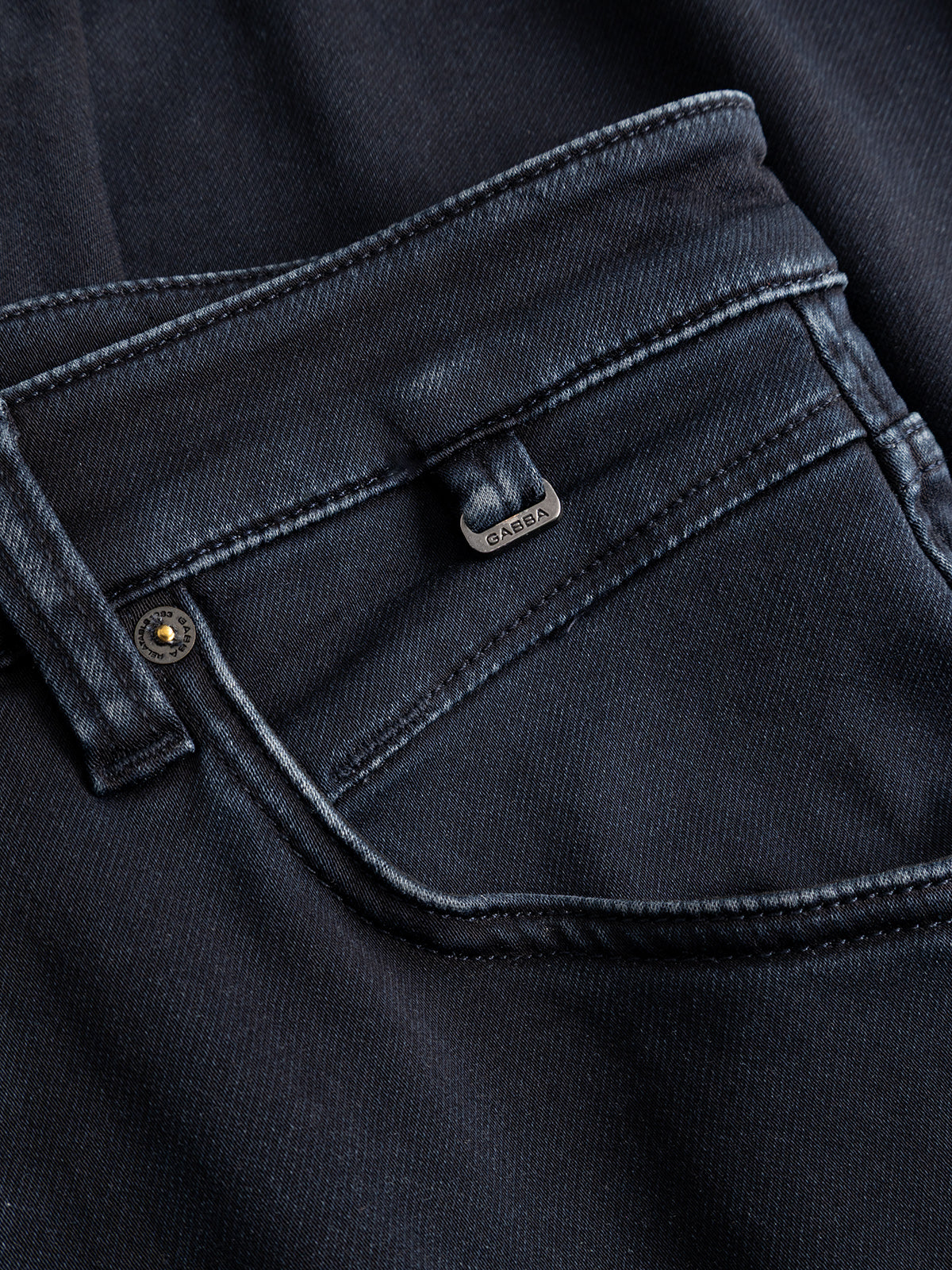 Close-up of a black denim jeans pocket with visible stitching, a metal rivet, and a small metallic tag labeled Gabba above the pocket. Crafted from premium indigo denim in a dark blue wash, the GABalex Cropped Torino RS2106 Jeans by Gabba feature a relaxed tapered fit for added comfort and style.
