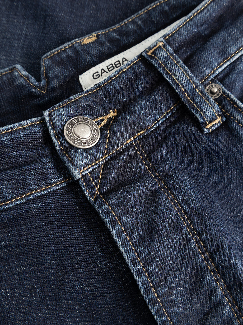 Close-up of the GABalex Cropped Cros RS2108 Jeans RCS in dark blue denim by Gabba, highlighting the metal button engraved with GABBA JEANS, yellow stitching, a belt loop, and a white waistband tag with the Gabba logo.