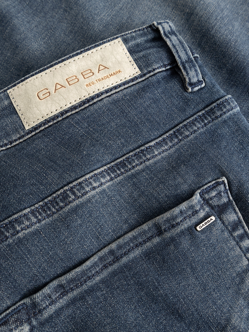 Close-up of the GABmarc Nham RS2113 Jeans in dark blue denim by Gabba, highlighting the back pockets crafted from ISKO stretch denim for performance comfort. One pocket features a white label with GABBA REG. TRADEMARK in light brown letters, while another displays a small black and white Gabba tag. The regular fit offers all-day ease and a classic silhouette.