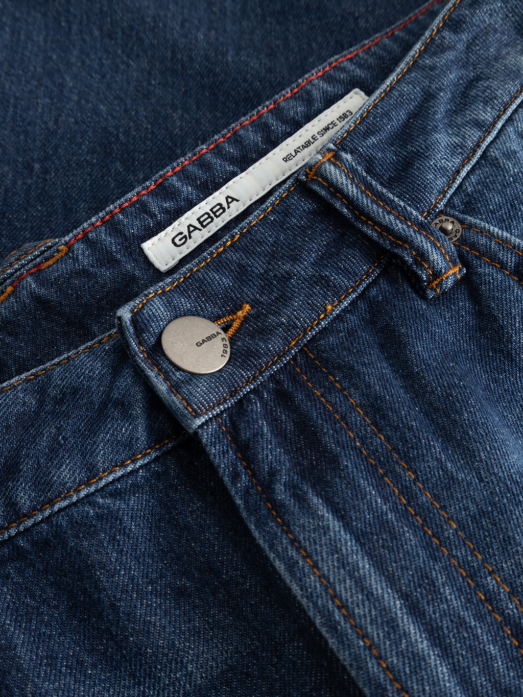 Close-up of the GABcarl Tona RS2101 Jeans in mid blue denim, crafted from organic cotton, featuring a metal button, belt loop, orange stitching, and a white Gabba label.