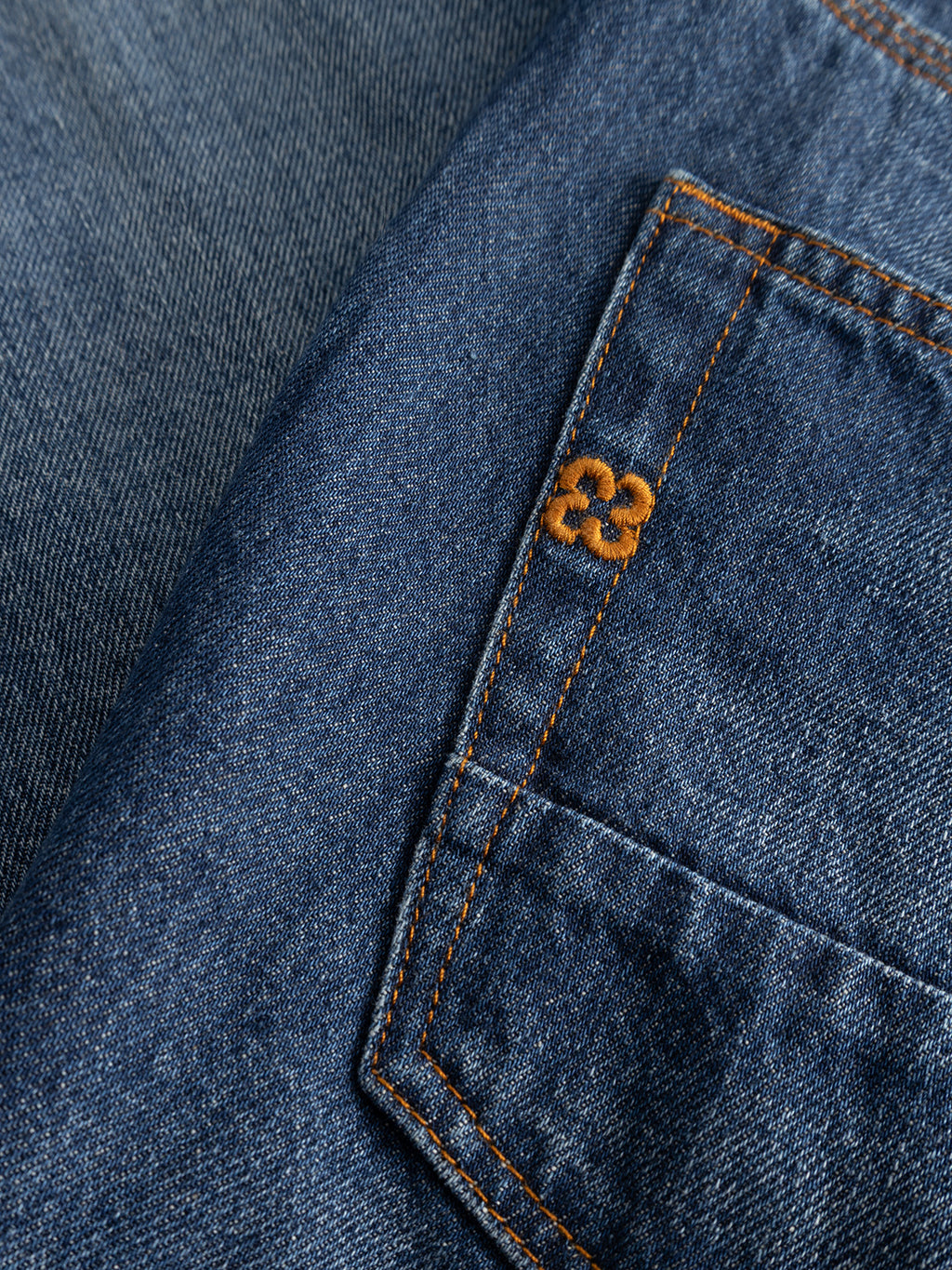 Close-up of Gabba GABcarl Tona RS2101 Jeans in mid blue denim, highlighting the small pocket with orange stitching and the number 23 embroidered on it. The texture of the organic cotton denim fabric is visible.