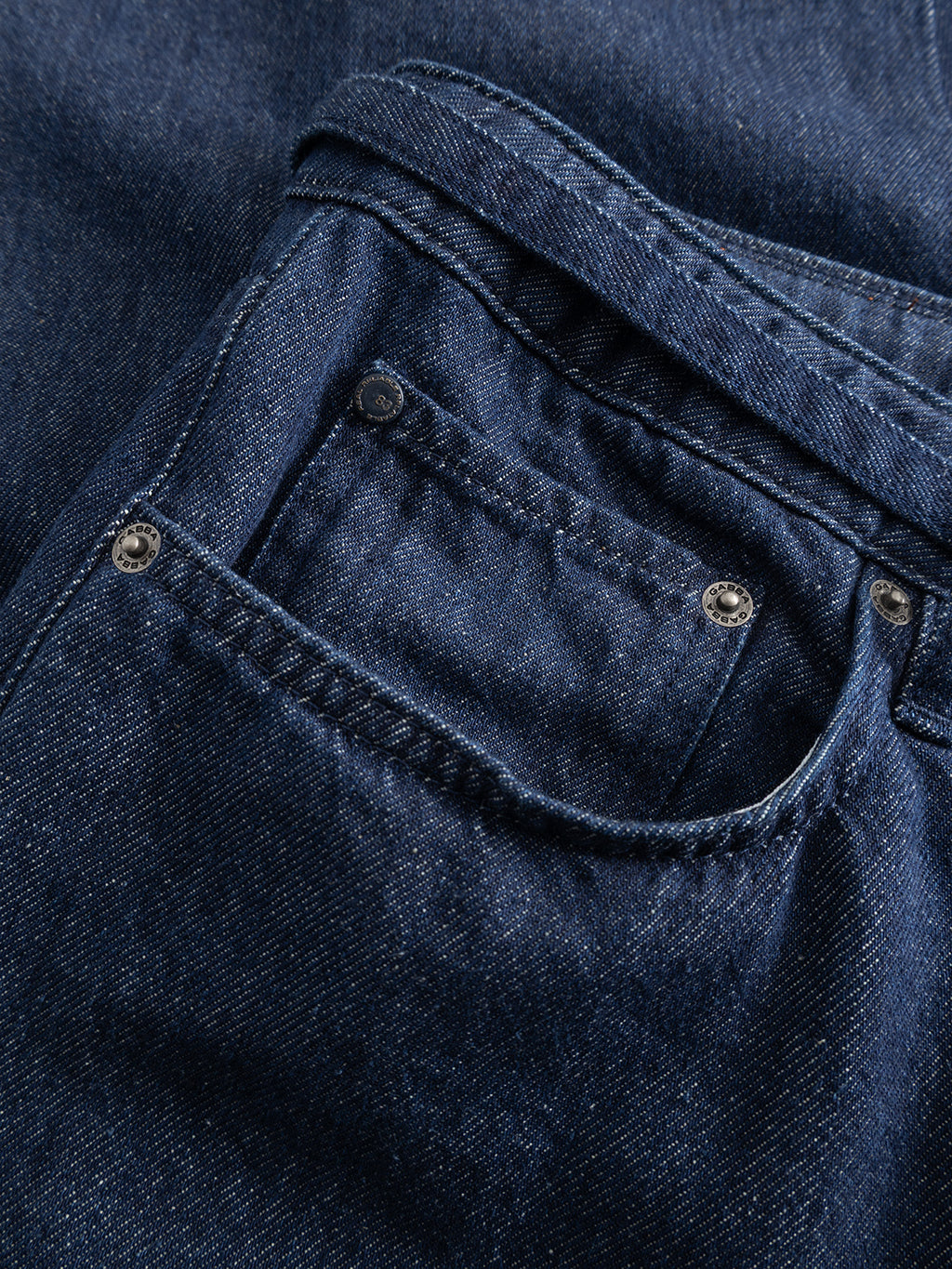 Close-up of the GABnoah Tona Rinse Jeans by Gabba in dark blue denim, showcasing the front pocket and coin pocket with visible stitching and metal rivets. Crafted from a rigid indigo organic cotton blend for lasting comfort and durability.