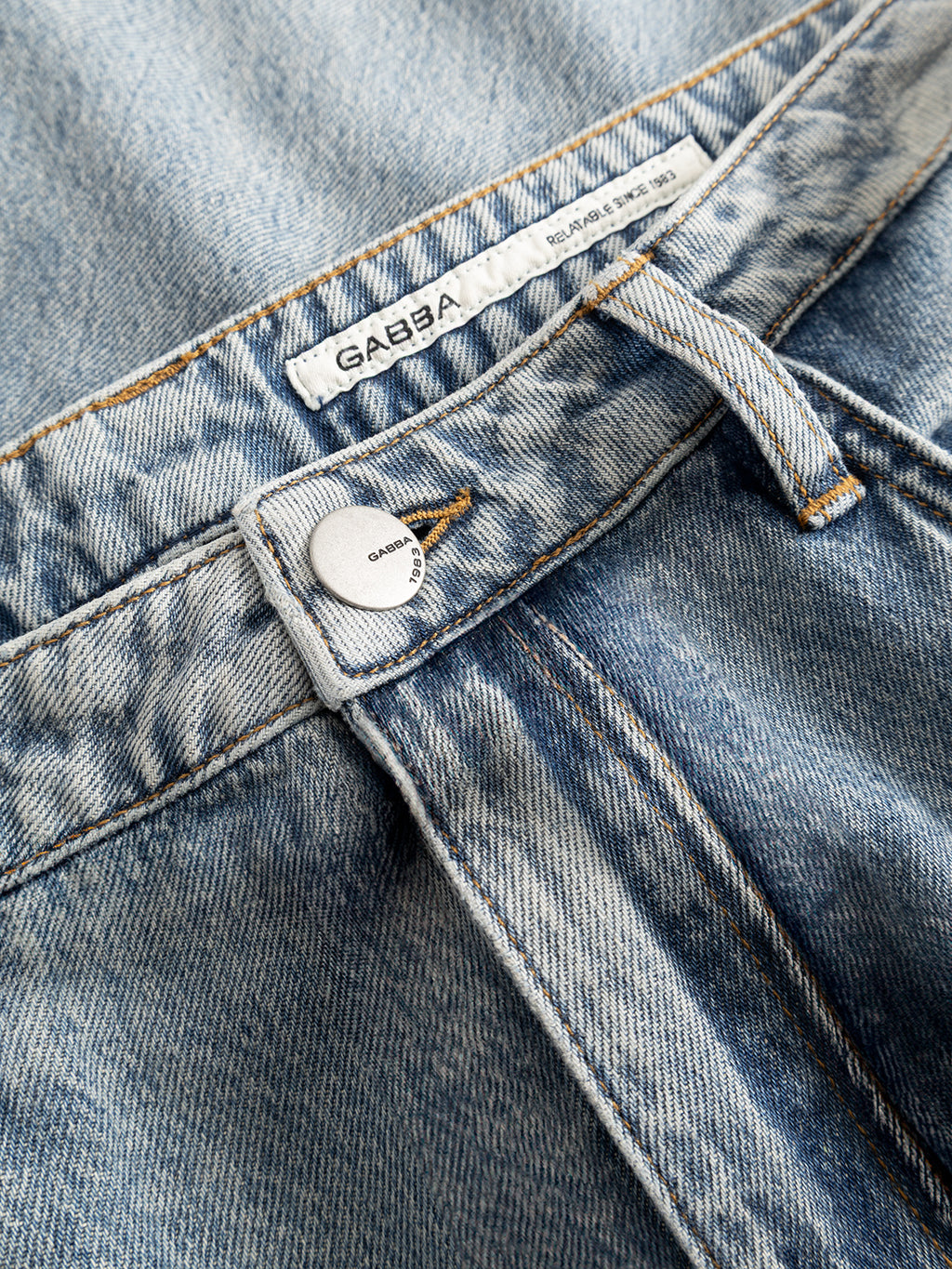 Close-up of the Gabba GABnoah Tona RS2100 Jeans in mid blue denim, showcasing a silver button and a white GABBA label. Crafted from rigid indigo organic cotton, these loose straight fit jeans feature visible stitching and fading that accentuate the fabric’s natural texture and detail.