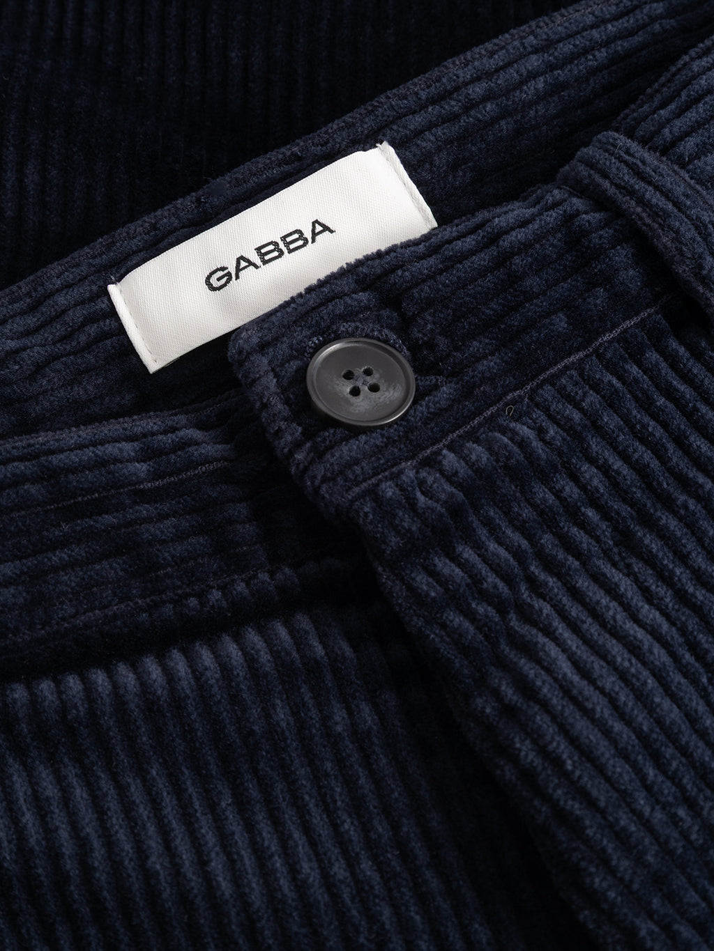 Close-up of the Gabba GABjoe Nopleats Ibre Pant in dark navy, showcasing stretch corduroy fabric, a black button, and a white Gabba label above the waistband, with classic chino-inspired construction for timeless style.