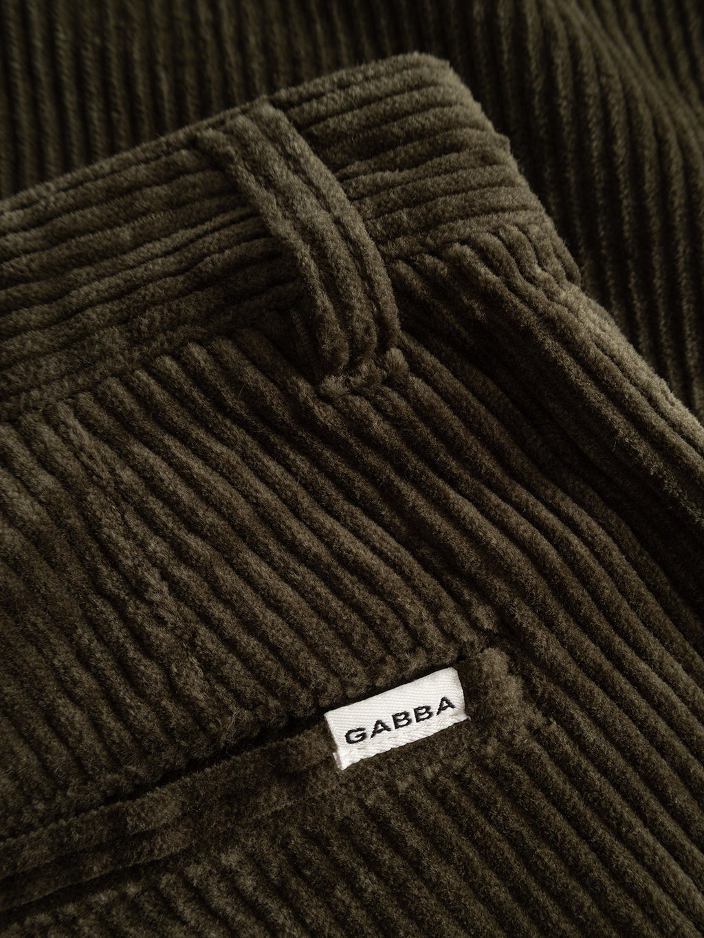 Close-up of the Gabba GABjoe Nopleats Ibre Pant in Forest Night, showcasing dark green stretch corduroy with vertical ridges, classic chino construction, a pocket detail, and a white label that reads Gabba.