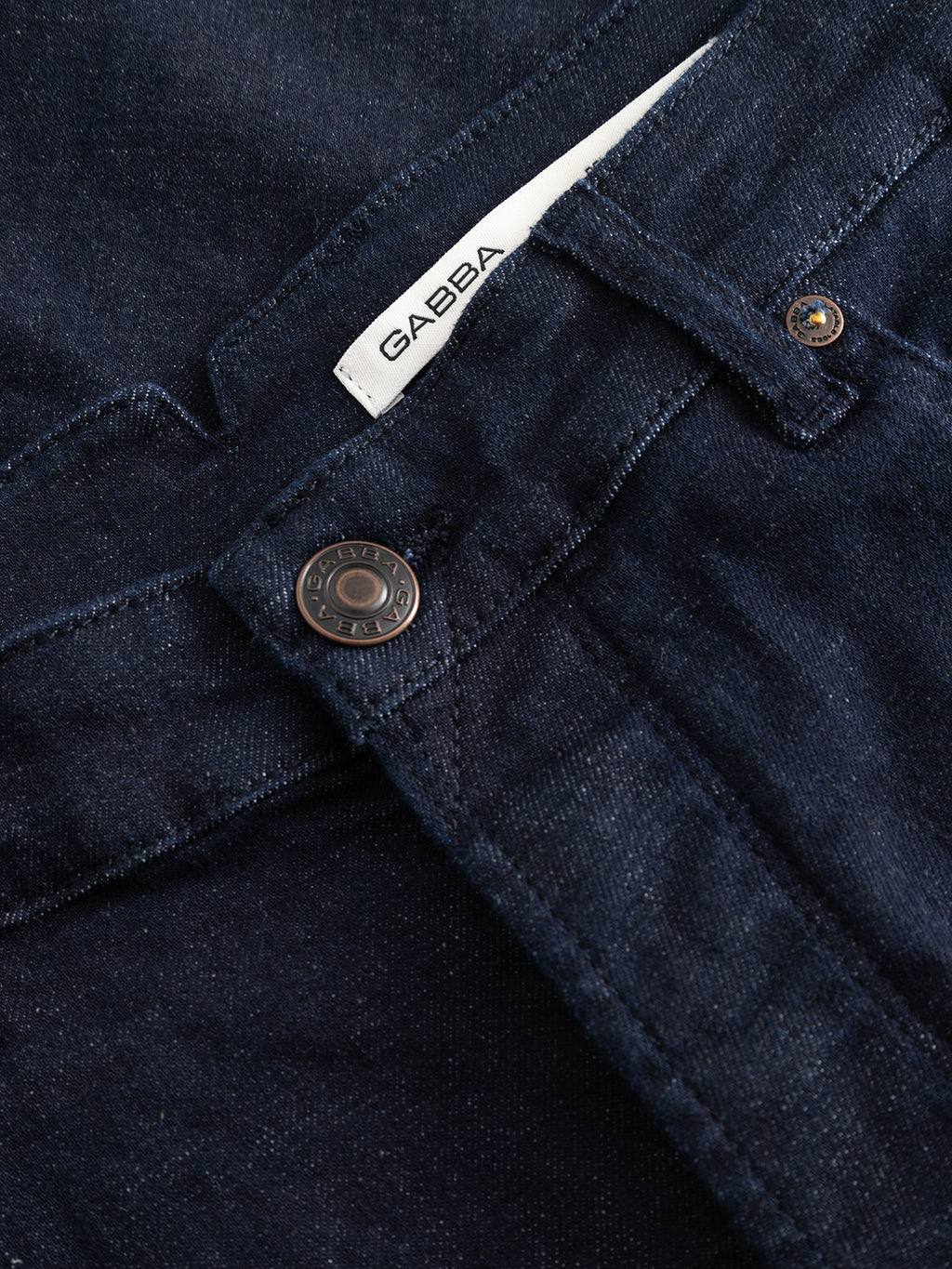 Close-up of the GABalex Cropped Bekham DS0001 Jeans by Gabba, crafted from dark blue denim in a dark rinse wash. Featuring a visible metal button, detailed stitching, and a white “Gabba” label above the waistband, these jeans are made from comfort stretch denim and offer a relaxed tapered fit for everyday ease.