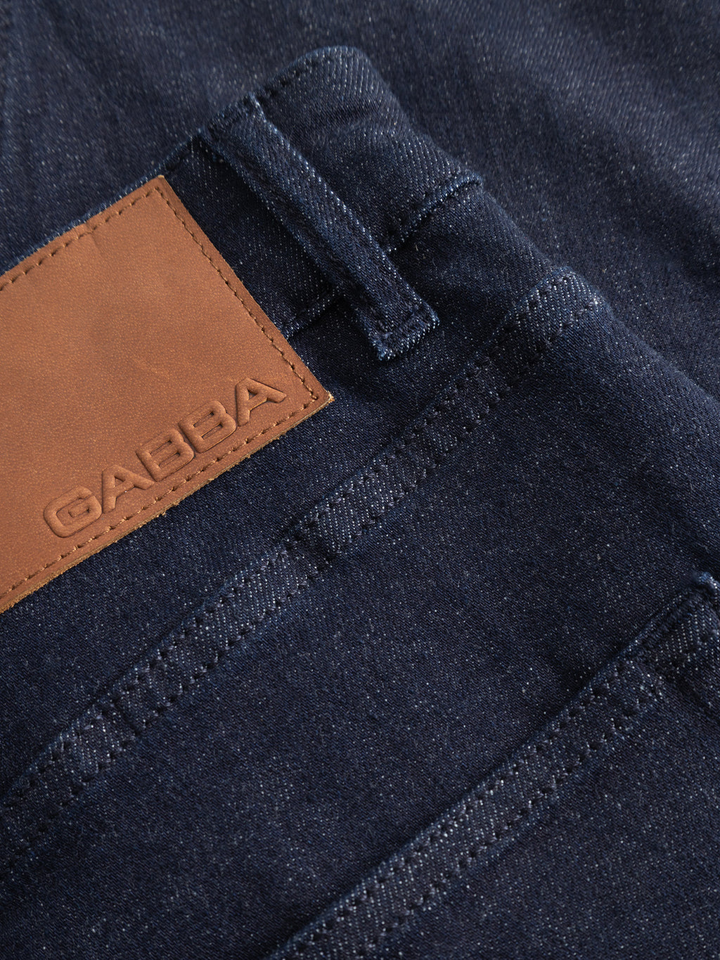 Close-up of the GABalex Cropped Bekham DS0001 Jeans by Gabba in dark blue denim, featuring a dark rinse wash. The image highlights the back pocket and a brown leather patch embossed with the Gabba logo, showcasing the comfort stretch denim texture and detailed stitching.