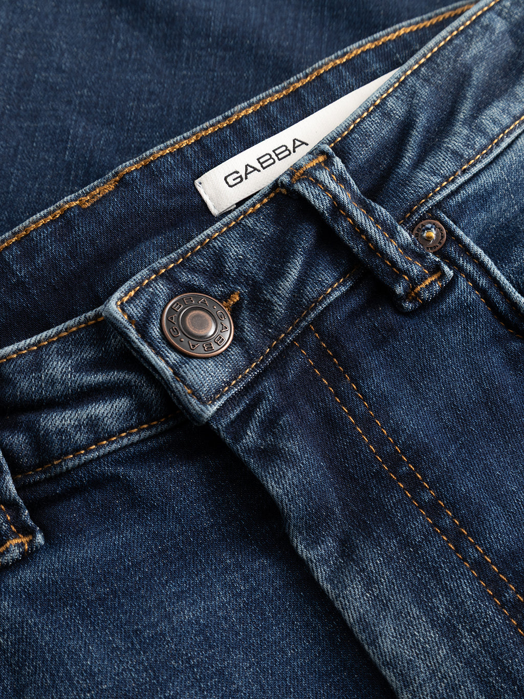 Close-up of the GABjones Bekham DS0002 Jeans in dark blue denim, featuring a metal button, orange stitching, and a white Gabba label above the waistband. Made from comfort stretch denim in a slim straight fit, these jeans offer easy movement and contemporary style.