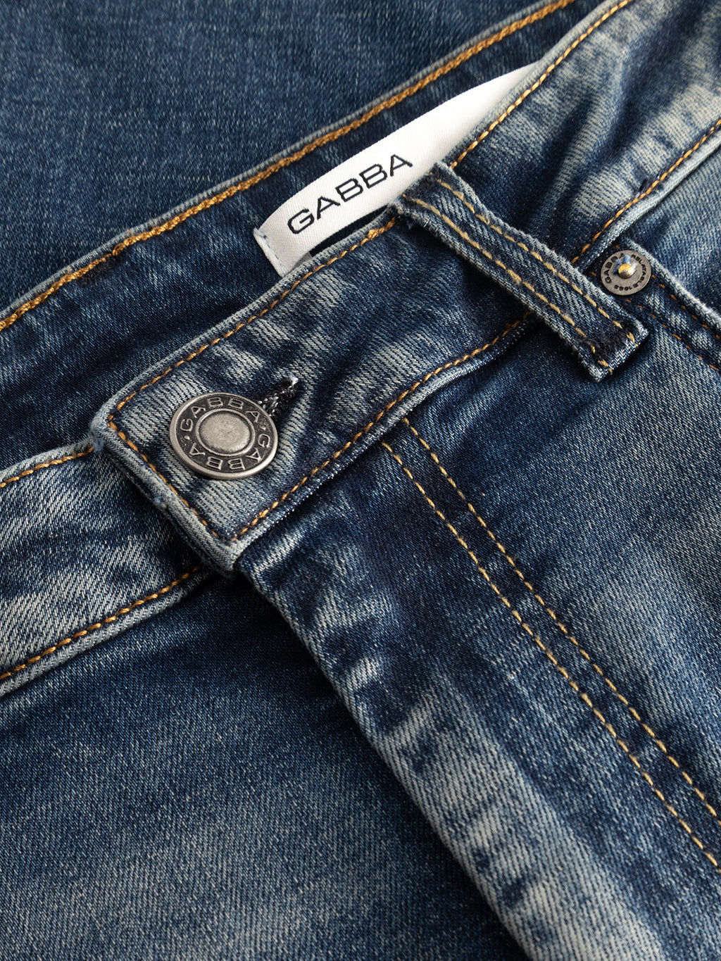 Close-up of the Gabba GABmarc Bekham DS0003 Jeans in mid-blue denim, featuring orange stitching, a silver button, and a white label with the Gabba logo inside the waistband. Made from comfort stretch denim, these jeans offer a classic regular fit designed for everyday ease.