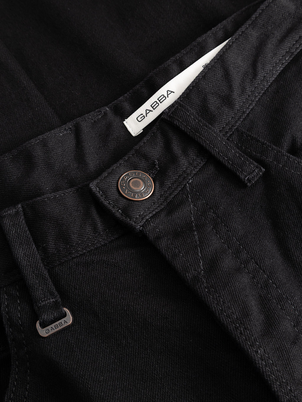 Close-up of the GABsenna Black DS0006 Jeans in black denim, showcasing a garment-dyed black finish, metal button, belt loops, and a white Gabba brand label. The fabric texture and detailed stitching are clearly visible.