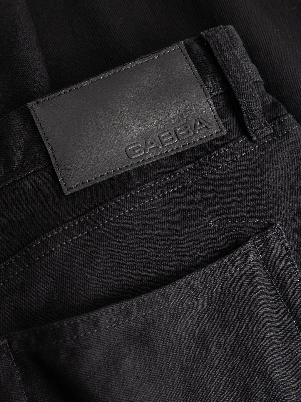 Close-up of the GABsenna Black DS0006 Jeans in black denim, featuring a black leather patch embossed with the Gabba brand name above the pocket and showcasing a garment-dyed black finish for added depth and sophistication.