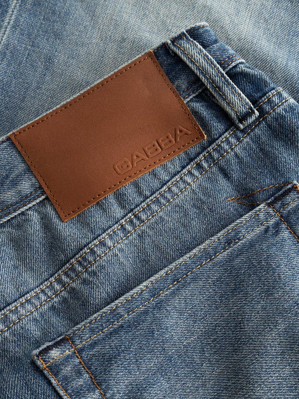 Close-up of the Gabba GABsenna Wolv DS0004 Jeans in dark blue denim, featuring a brown leather patch with embossed branding above the back pocket. Distinct yellow stitching details accent the pocket and belt loop.