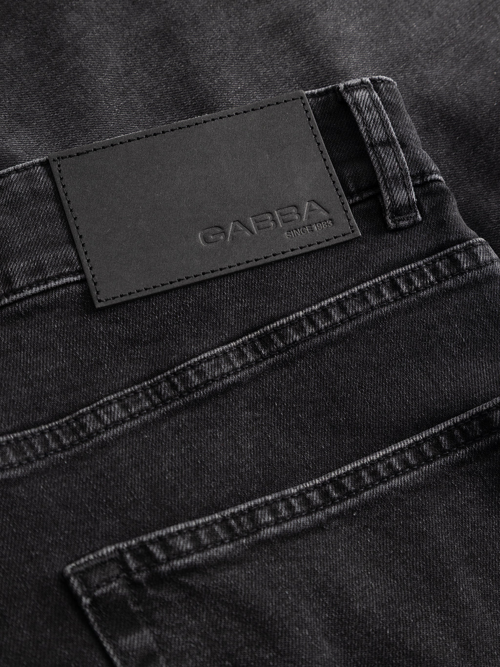 Close-up of the back pocket and waistband of the GABalex Cropped Blerb WW0031 Jeans in black denim by Gabba, crafted from high-density black denim and featuring a black leather patch embossed with the Gabba brand name and the text “Since 1983.” The fabric texture, washed black finish, and precise stitching are clearly visible.