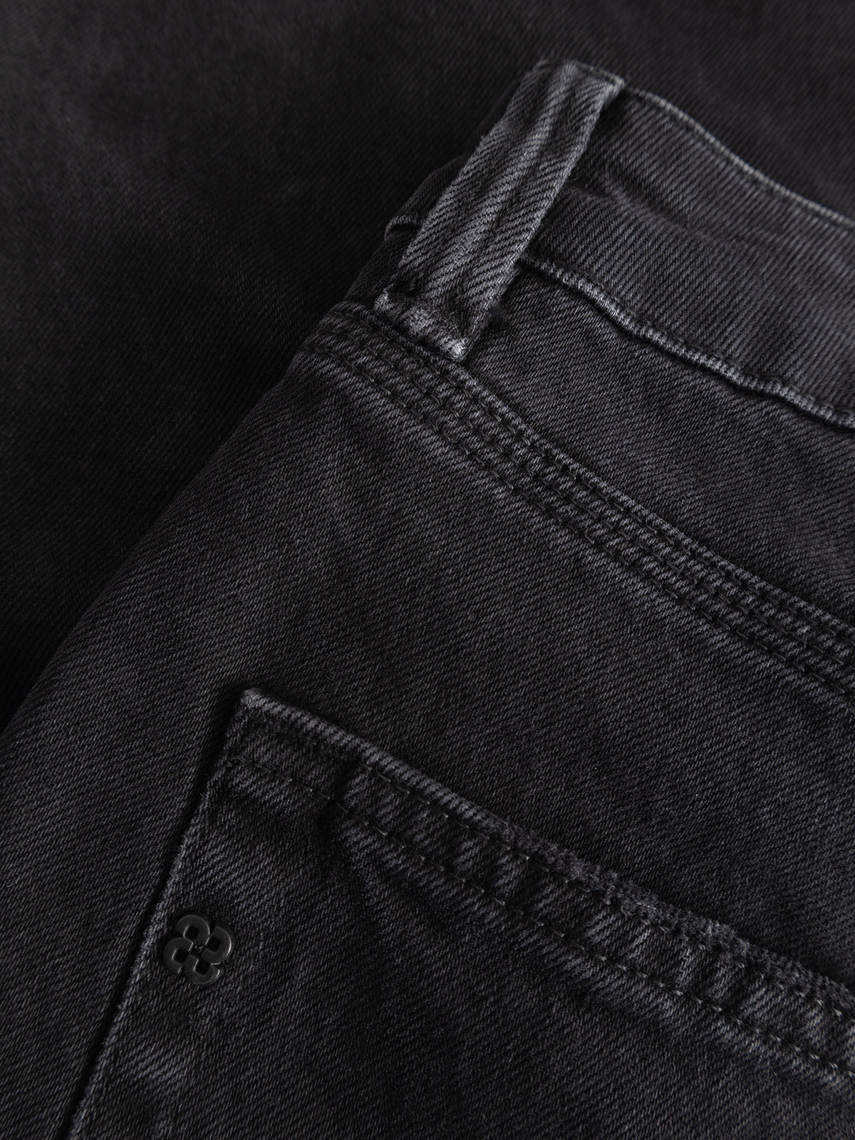 Close-up of the Gabba GABcarl Blaccom WW0035 Jeans in black denim, showcasing the back pocket, waistband, and detailed stitching. The fabric texture highlights the relaxed feel and loose tapered fit of these jeans. The pocket is accented with a small metal rivet featuring a four-leaf clover design.