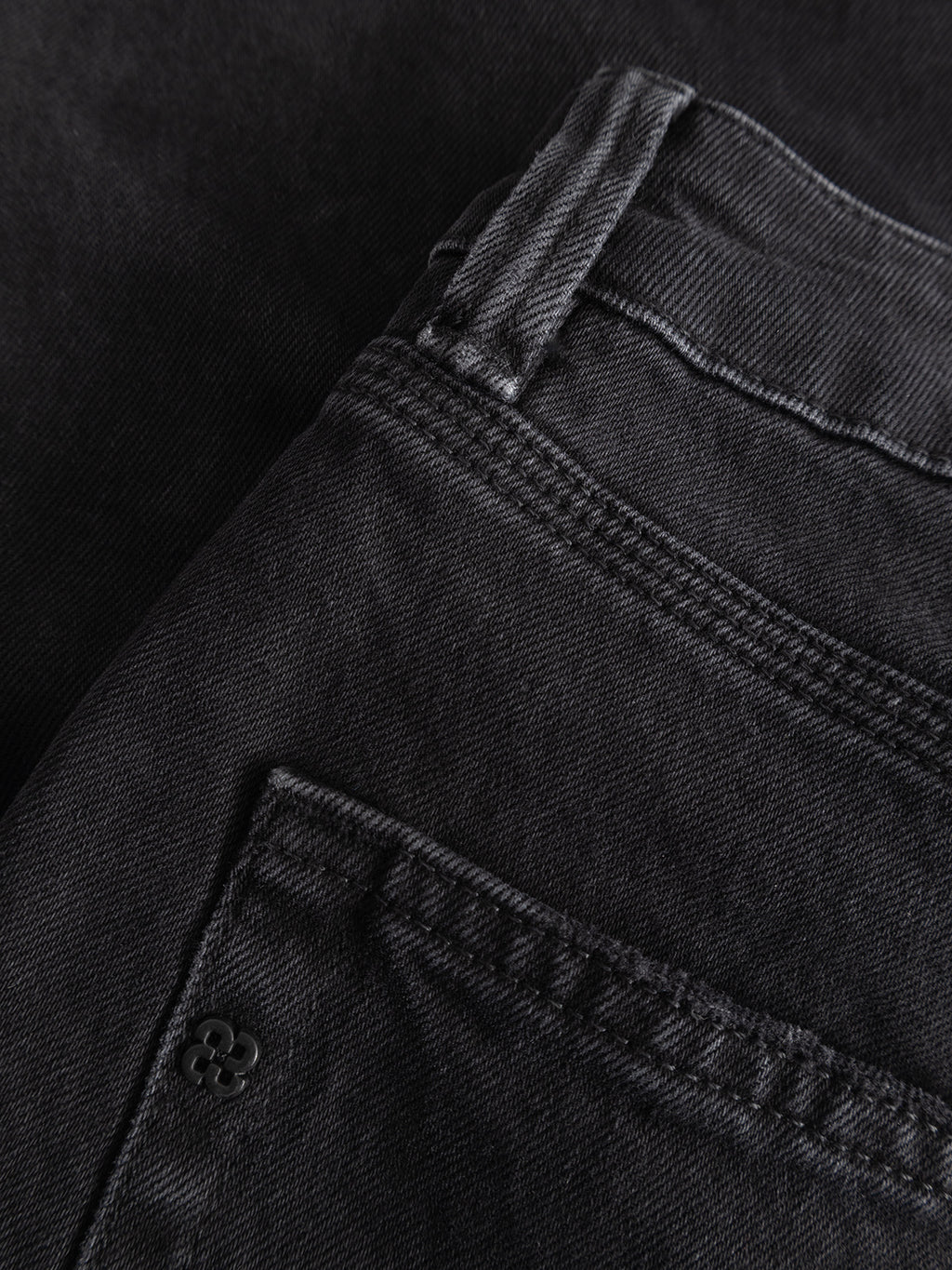 Close-up of the Gabba GABcarl Blaccom WW0035 Jeans in black denim, showcasing the back pocket, waistband, and detailed stitching. The fabric texture highlights the relaxed feel and loose tapered fit of these jeans. The pocket is accented with a small metal rivet featuring a four-leaf clover design.
