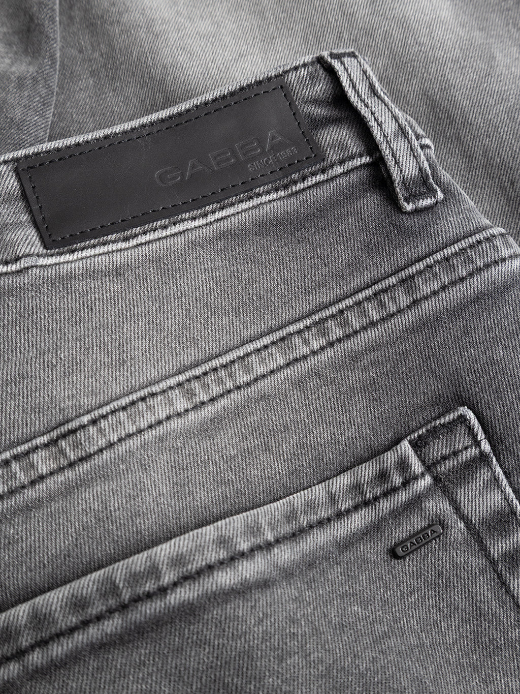 Close-up of GABmarc Blerb WW0032 Jeans in grey denim, featuring comfort stretch fabric, detailed stitching, and back pockets with a black leather patch embossed with the Gabba brand name. Fabric texture and stitching details are clearly visible.