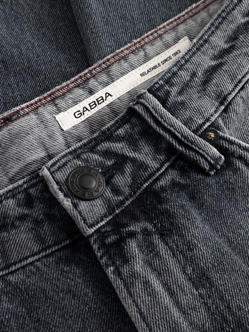 Close-up of the GABmax Primesto WW0030 Jeans by Gabba, crafted from heavy 3x1 grey denim and featuring a black metal button, detailed stitching, and a white label with the Gabba logo and “Relatable Since 1983.” These modern straight fit jeans showcase a distinctive stone grey wash for a contemporary style.