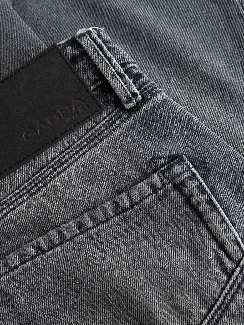 Close-up of Gabba GABmax Primesto WW0030 Jeans in grey denim, showing the back pocket, waistband, and a black rectangular leather patch with embossed branding. The stone grey 3x1 heavy denim fabric texture and detailed stitching are clearly visible, emphasizing the modern straight fit design.