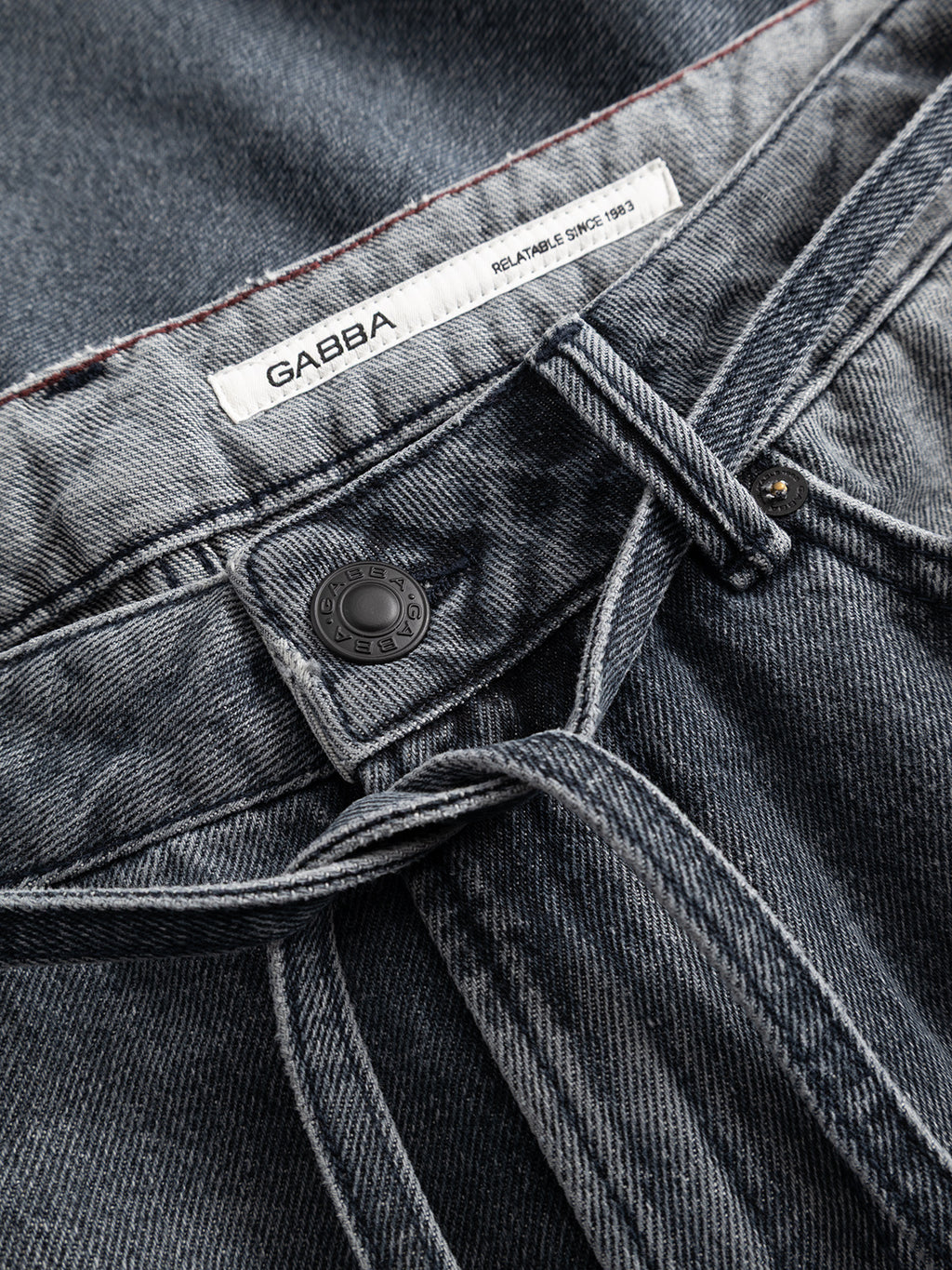 Close-up of a pair of GABnoah Primesto WW0030 Jeans in grey denim by Gabba, featuring a visible button, belt loops, and a white label reading GABBA on the inside waistband. The fabric texture and stitching details are clearly shown, highlighting the quality construction of these loose straight fit jeans.
