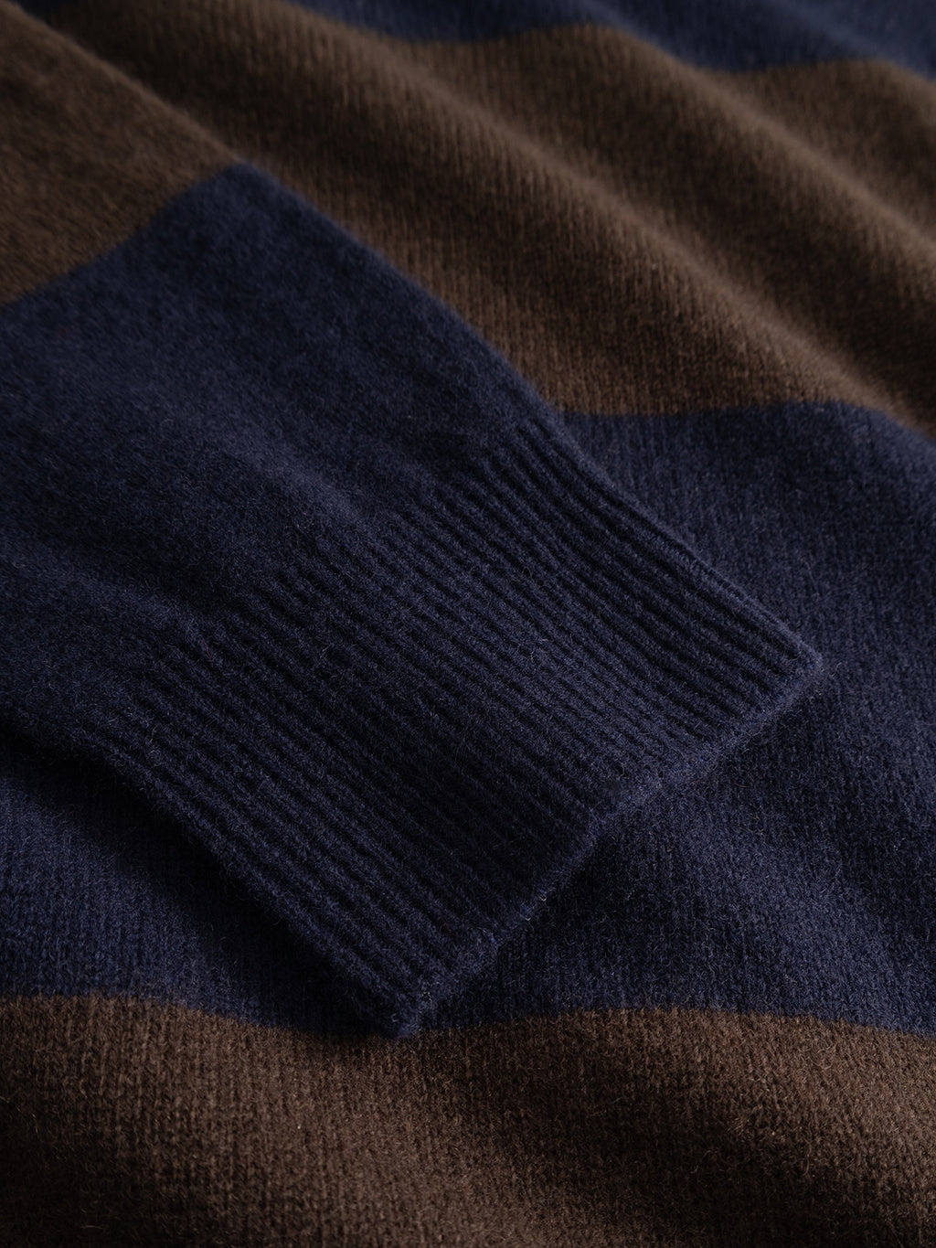 Close-up of the Gabba GABworren Polo Stripes Aico LS Knit in Brown Stripe, showcasing wide horizontal navy blue and brown stripes and the ribbed cuff of a sleeve resting on the soft wool polo fabric.