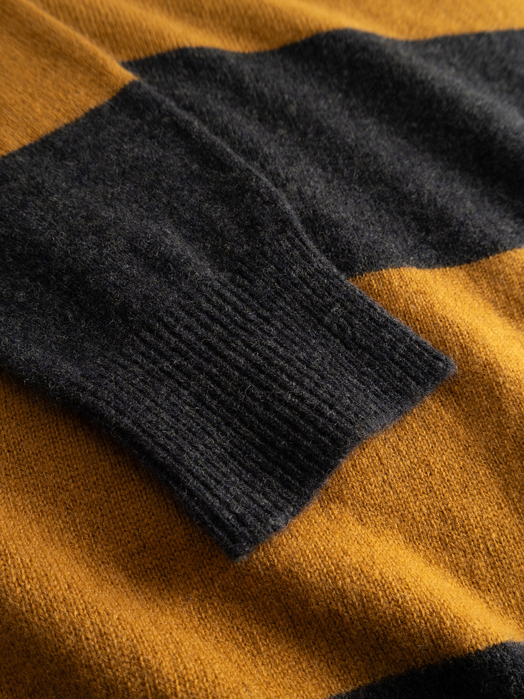 Close-up of Gabba’s GABworren Polo Stripes Aico LS Knit in yellow stripes, highlighting the wide horizontal mustard yellow and dark gray stripes. The image showcases the textured knit fabric and detailed stitching of this men’s regular fit sweater.