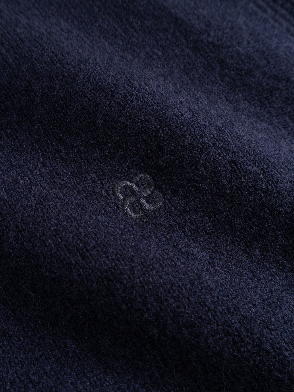 Close-up of dark navy blue textured fabric from the Gabba GABworren Polo Aico LS Knit sweater, featuring a small, subtle embroidered abstract logo at the center.