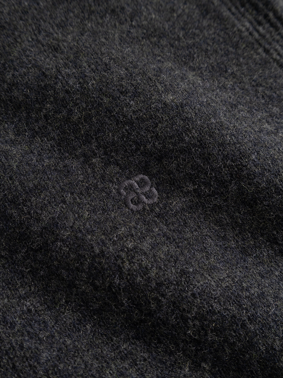 Close-up of the Gabba GABworren Polo Aico LS Knit in Dark Grey Mel—a men’s regular fit sweater crafted from soft, slightly fuzzy wool knit. It features a ribbed polo collar for refined detailing and a small, subtle embroidered logo with two interlocking shapes at the center.