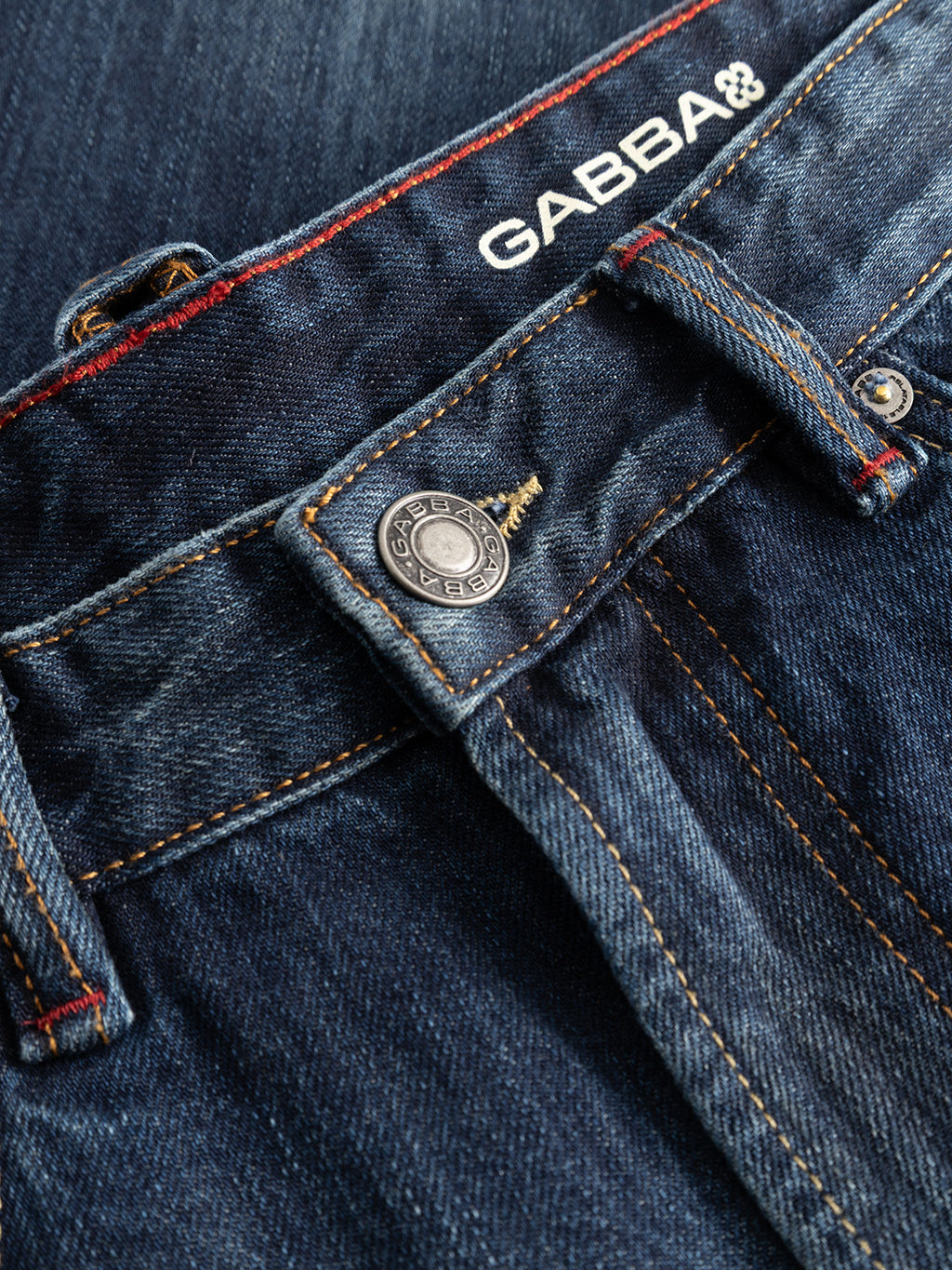 Close-up of the GABcarl Selvedge DS0005 Jeans in dark blue denim, crafted from recycled cotton selvedge denim with orange stitching, a metallic button, belt loops, and the Gabba brand name printed on the waistband.