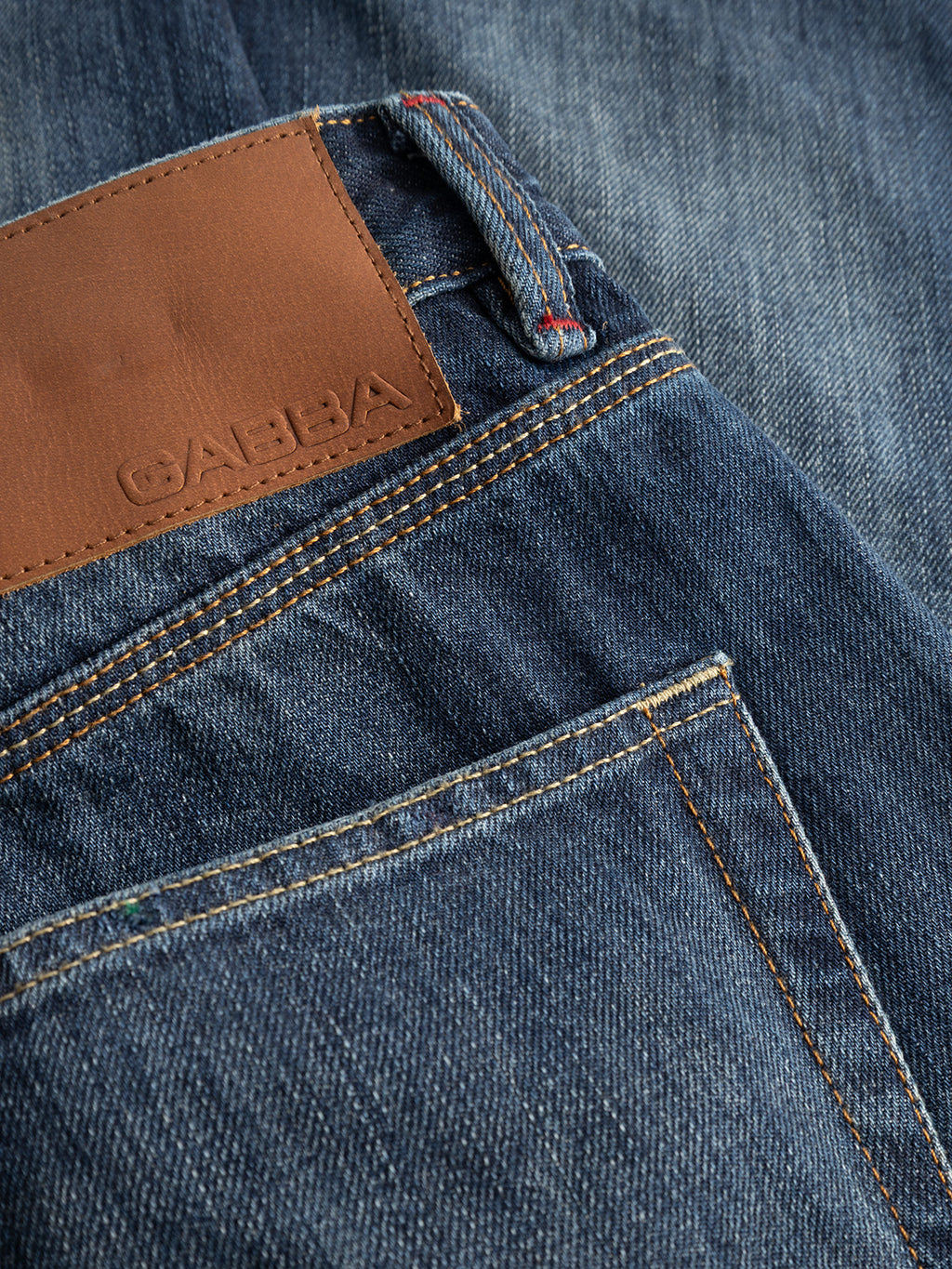 Close-up of the GABcarl Selvedge DS0005 Jeans in dark blue denim by Gabba, showcasing the brown leather patch embossed with the brand name above the back pocket. Featuring clearly visible stitching details, these jeans are crafted from Candiani recycled cotton selvedge denim and offer a loose tapered fit for modern comfort and style.