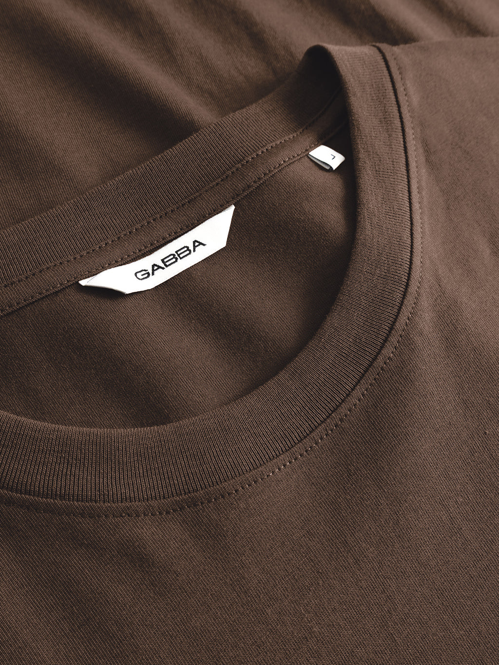 Close-up of the Gabba GABdune Element GOTS SS T-Shirt in Brown Slate, showcasing a white label with the Gabba brand name sewn inside the collar. The fabric appears soft and neatly stitched.