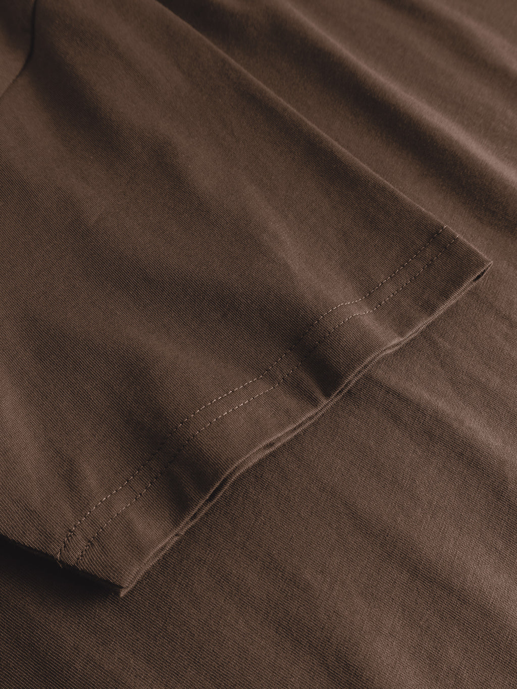 Close-up of the GABdune Element GOTS SS T-Shirt - Brown Slate by Gabba, featuring the sleeve lying flat on matching brown fabric and highlighting the detailed hem stitching.