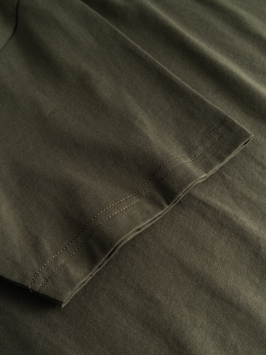 Close-up of a Gabba GABdune Element GOTS SS T-Shirt in Forest Night, classic fit, with sleeve lying flat on matching fabric and showing stitching detail along the hem.