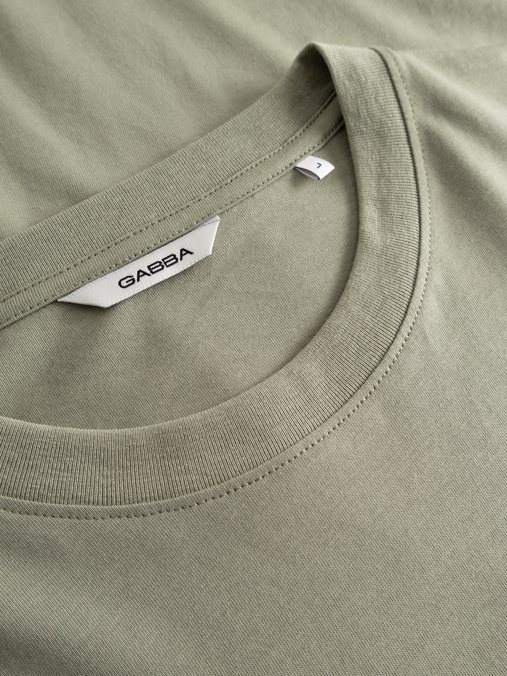 Close-up of a classic fit, light green organic cotton GABdune Element GOTS SS T-Shirt by Gabba, shown flat with a round neckline and a white label displaying the Gabba brand and an L size tag.