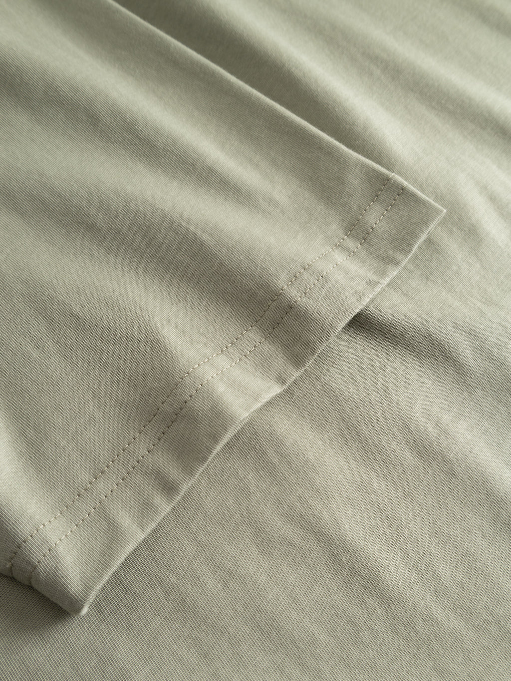 Close-up of the light green GABdune Element GOTS SS T-Shirt by Gabba, highlighting the hem and stitching on this classic fit organic cotton tee, with visible soft folds and a smooth texture.