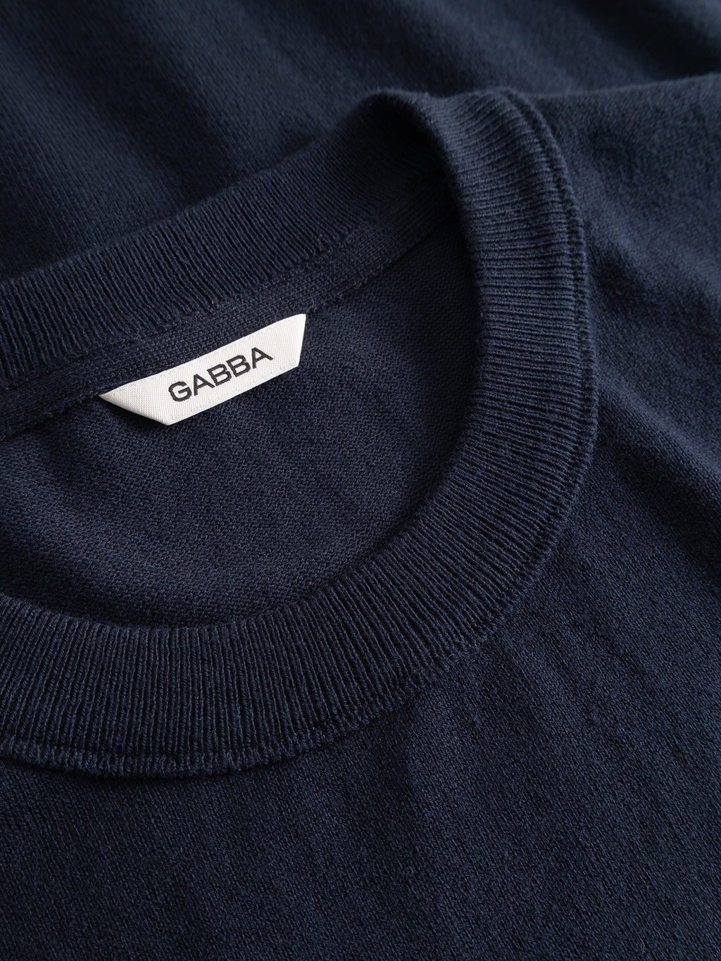Close-up of the ribbed crew neckline of a navy GABfumo Element Spy LS Knit long-sleeved flat-knit cotton shirt with a brand tag inside the collar.