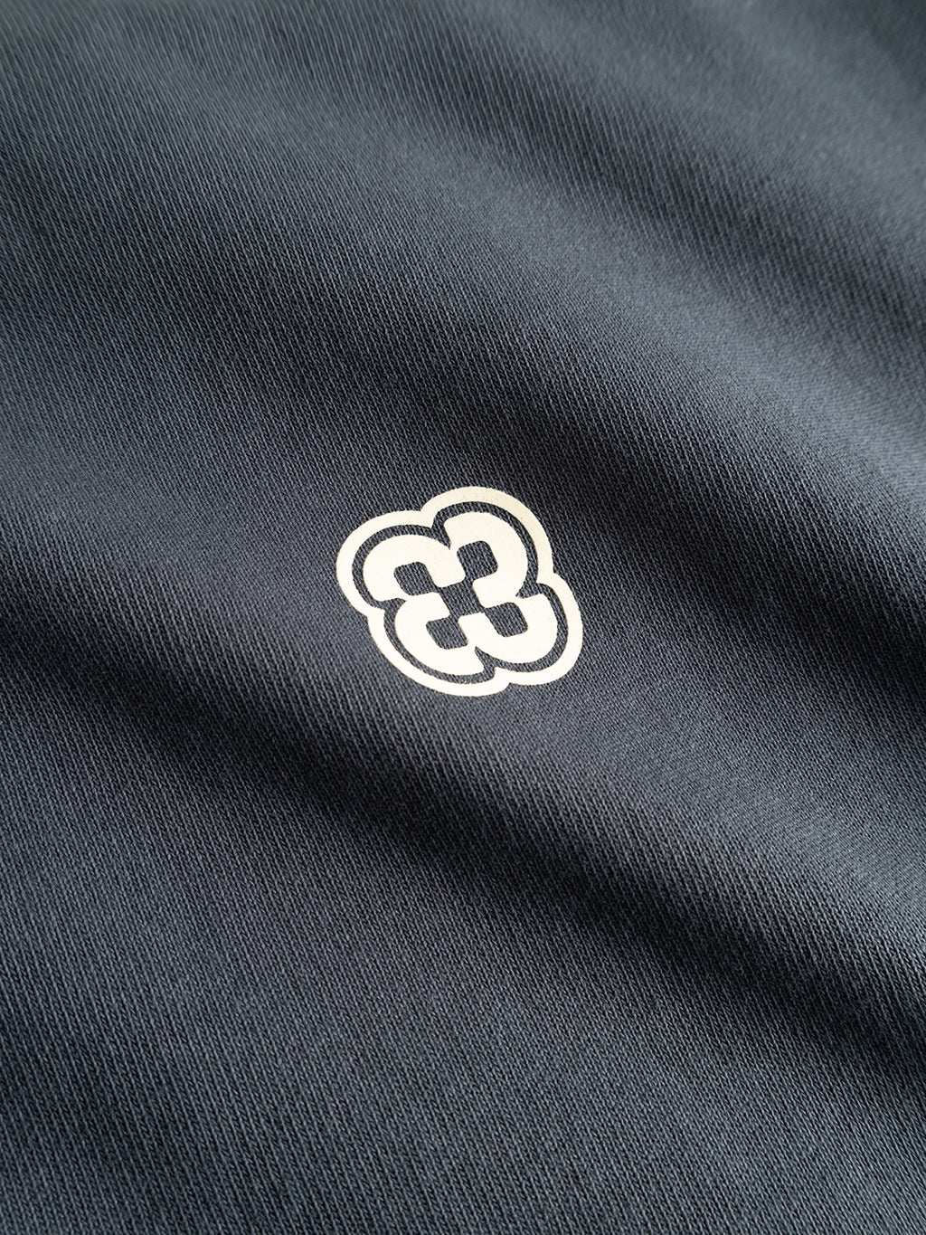 A close-up of the Gabba GABlegin Wix Chap Boxy Hour SS T-Shirt in Turbulence Blue, crafted from heavyweight cotton with a small white abstract geometric interlocking logo printed at the center.