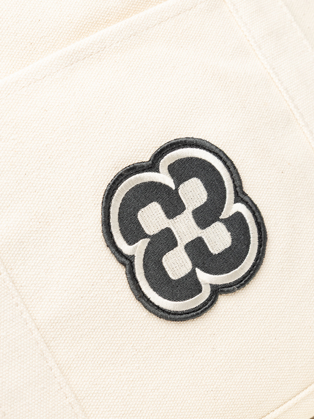 A close-up of the GABchap Tote Bag - Off White by Gabba, showcasing a black and white embroidered geometric flower-like pattern on its cream fabric background.